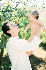 Man in a white shirt raises a baby in his arms