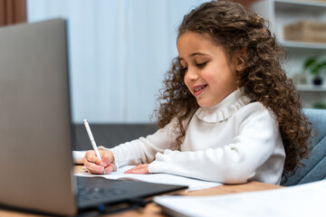 Smiling little caucasian girl writing something attentively while using laptop