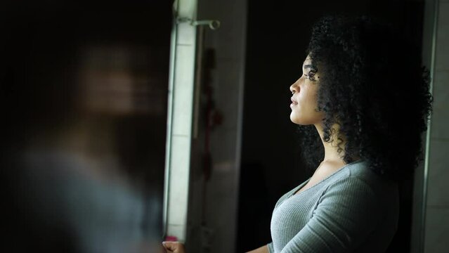 A contemplative young woman standing by window looking outside