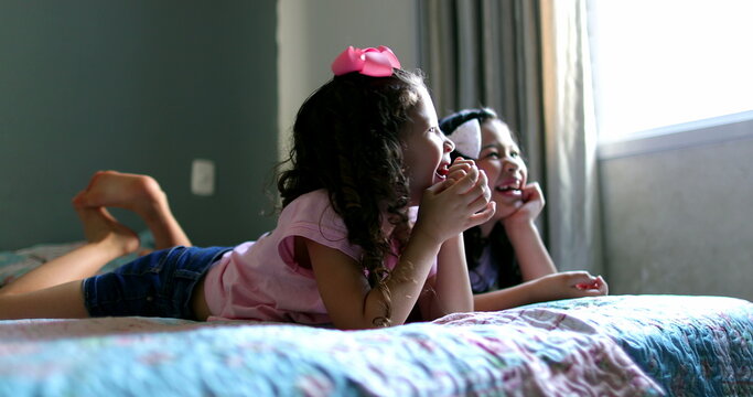 Two little girls watching TV screen in bed laughing and smiling