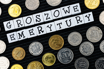 The wording "groszowe emerytury" translated as "penny pensions" and many Polish coins on the black background. New taxation rules in Poland. Photo taken under artificial, soft light