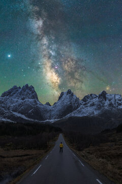 Unrecognizable traveler on road against mountains under starry sky at night