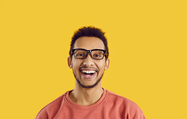 Headshot of student with happy face expression isolated on solid yellow background. Studio portrait of cheerful excited young black man in glasses looking at camera, smiling and laughing sincerely