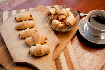 Croissants with apple jam and a cup of coffee on a wooden background.