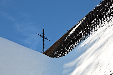 An iron cross on the shingle roof of an old church