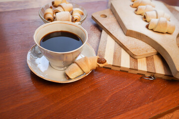 Croissant with apple jam sprinkled with powdered sugar with a cup of coffee on a wooden background.