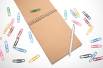 Top view of open spiral blank notebook with pen on white desk background with paper clips. Writing tools. Office supplies.