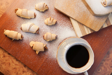 Croissant with apple jam sprinkled with powdered sugar with a cup of coffee on a wooden background.