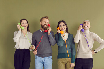 Happy diverse businesspeople isolated on green studio background talk on corded phone. Smiling...