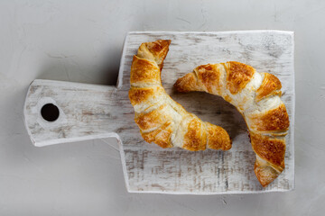 two freshly baked ruddy croissants lie on a rough birch cutting board on a light concrete background surface. top view
