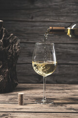 Bottle of white wine poured into the wine glass, on wooden background. Vertical format. Beverage and wine concept.