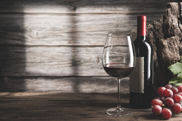 Elegant glass of wine and red wine bottle with grapes and shadows next to the window  on dark wood background with copyspace.