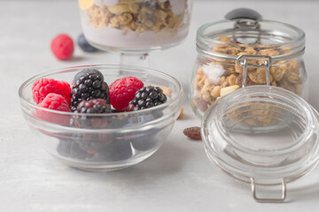 Ingredients for a homemade natural dessert. Granola with raspberries, blueberries, yogurt. Glass jar with muesli on a light background. Close-up. Selective focus.