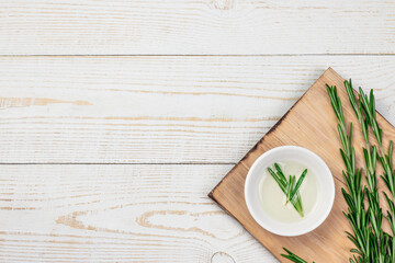 Fresh rosemary branches on cutting board with organic oil, over white isolated background with copy space.