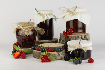 Different seasonal berry jam in jars and empty round natural wooden podium for your products on white background.