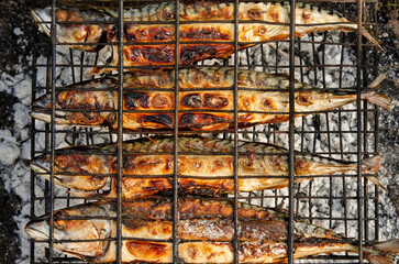 Delicious grilled mackerel fish inside grill grid on charcoal grill brazier