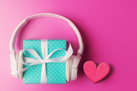 Blue gift box with headphones and Valentines heart on pink background with copy space