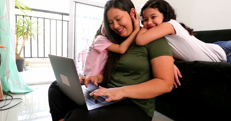 Mother multi-tasking, using computer laptop at home while parenting two children, staying at home. real life mom working and parenting