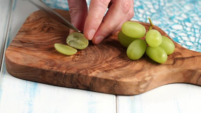 Green grapes without seeds are cut into quarts on a wooden board made of olive wood.