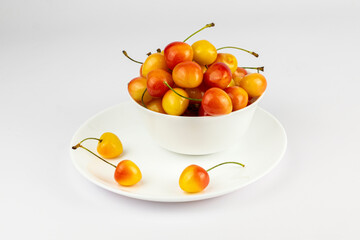 Ripe sweet rainier cherries in a white bowl and on plate on white background.