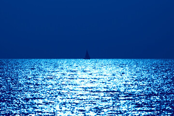 Silhouette of a sailing boat in sunset sunrise time on the open sea waters.