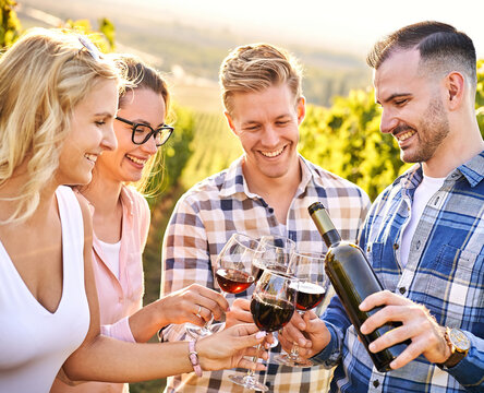 Young friends having fun outdoors - Happy people enjoying harvest time together at farmhouse winery countryside - Youth and friendship concept - Tasting red wine at vineyard before sunset
