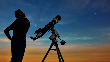 Silhouette of a man, telescope and countryside under the starry skies.