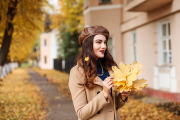 Romantic woman with autumn leavrs bouquet spending time outdoors in the city street in fall season.