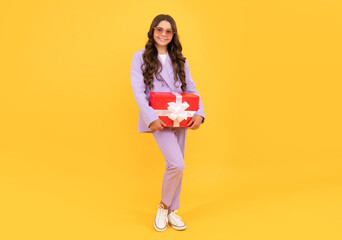 trendy cheerful teen girl in sunglasses and suit hold giftbox full length, occasion