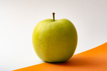 Green apple on orange and white background concept design. Education, health and healthy eating concept.