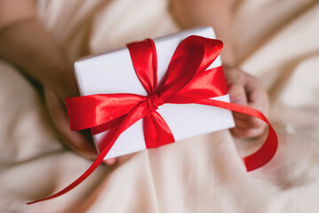 Children's hand with gift on a white bed to Christmas, Valentine's day, Mother's Day.