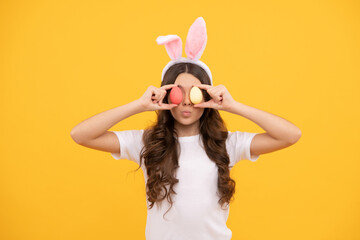 funny teen girl in bunny ears hold eggs on yellow background, easter