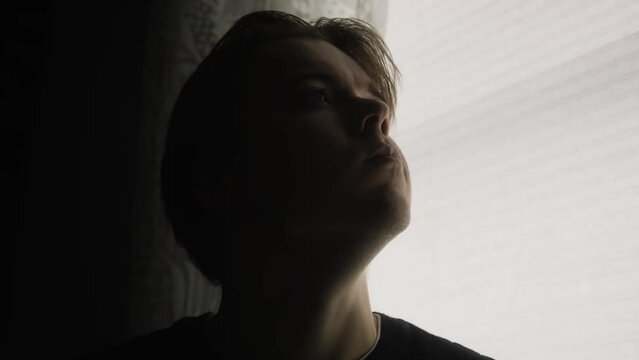 Young handsome white man looking for satisfaction and hope. He is questioning his life in his dimly lit bedroom. The moody cinematic atmosphere, adds tension and mystery. 