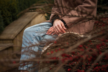 Fototapeta premium Woman in jeans and coat crossing hands sitting on plaid on steps railing in city park in early spring
