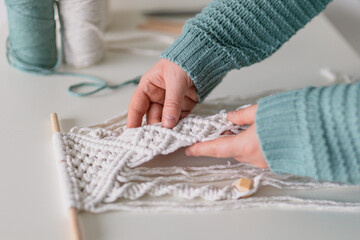 Hand of a woman when she is making macrame. Natural cotton threads and wooden beads. Handmade macrame belt in work process. Female hobby.