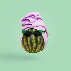 Funny stylish attractive watermelon in sunglasses and a towel on a green background.