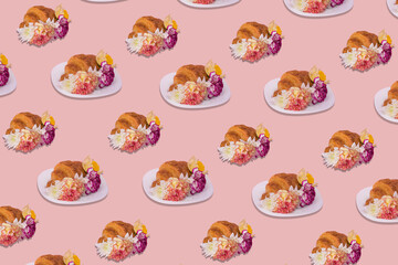 Creative pattern made of freshly baked croissant with various colorful flowers on pastel pink background.