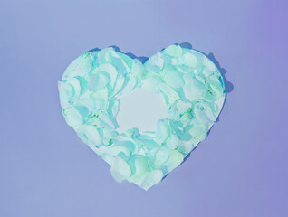 A heart silhouette made of green rose petals on pastel blue background. Minimalist concept of love and affection. Valentine's Day pattern. Anniversary, love, wedding. Copy space. Flat lay.