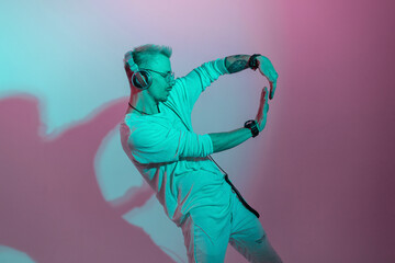 Stylish fashionable handsome man hipster listening to music on headphones and dancing in studio with pink and blue light