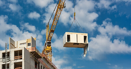 A Crane is lifting a wooden building module to its position in the structure. Construction site of...