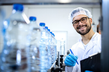 Smiling technologist working in bottling factory controlling production of drinking water and PET...