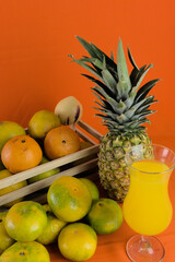 glass of juice and tropical fruits on orange color background