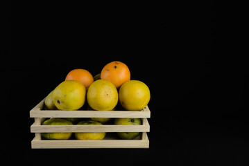 oranges contained in a small wooden box with a black background. image of fresh oranges