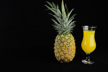 glass of juice with pineapple on black background