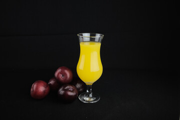 glass of juice with red plums on a black background