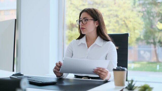 Video of beautiful business woman working with computer while cheking some documents in modern startup office.