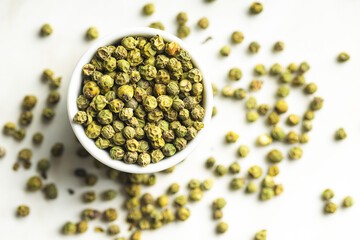 Dried green peppercorn. Dry green pepper spice in bowl on a white table.