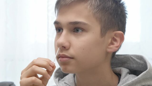 Teenage boy taking antigen self-test for Covid-19 with rapid diagnostic test kit. Kid using nasal swab while doing coronavirus PCR test at home before go to school lessons