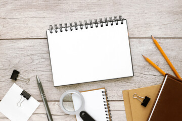 Open spring notepad with white note and drawing paper next to pencil and notepads. Distressed wood background, top view.