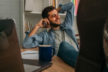 man at home relaxed with computer talking on mobile phone